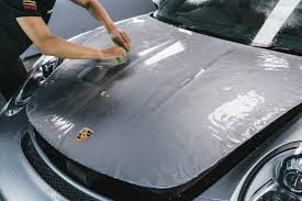 A close-up of a hand applying clear paint protection film to a car's glossy surface.