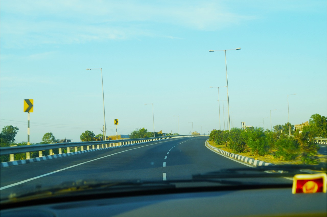 A long, straight highway stretches through a vast desert landscape, flanked by rugged mountains under a bright blue sky with scattered clouds- Is ceramic window tint worth it​